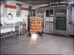 Meat processing facility displays rack of sausage resting over USDA approved flooring.