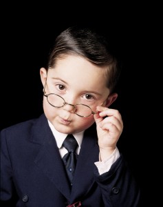 A boy dressed as an executive gives a judgmental look over rim framed glasses.