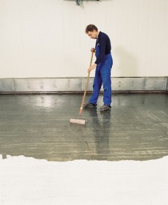 Man with roller in blue overalls paints flooring with acrylics.