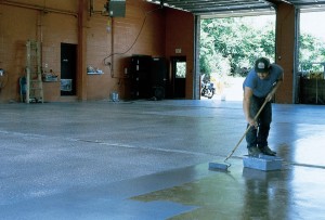 Contractor spreads non toxic floor sealer over large warehouse concrete floor.