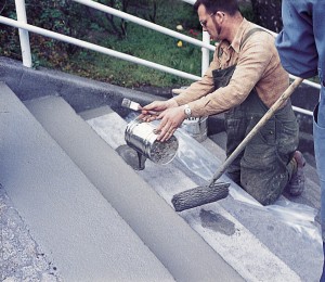 Two men paint gray acrylic on stairs leading from the floor above.