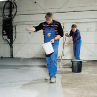 Contractor sprinkles acrylic impregnated product to floor surface during installation.