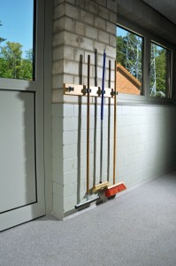 Brooms and squeegee hang in wait to clean a dog kennel floor grating system.