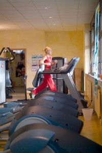 Woman jogs on row of treadmills covering this home gym floor space.