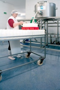Worker stacks product on rack while standing on blue colored acrylic concrete floor system.