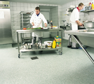 Grey coated flooring system covers concrete subsurface in commercial kitchen with prep cooks.