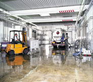 Concreted high gloss seal coats industrial floor with large tanker truck and forklift casting reflection across.