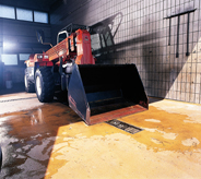 Oversized bulldozing truck sits atop durable orange colored flooring.