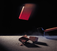 A brick falls atop swinging hammer to demonstrate floor coating durability.