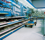 Highly trafficked walkway area of hardware store displays loaded rolling cart atop grey covered flooring.