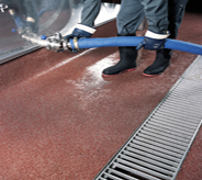 Worker attached large hose to stainless steel tank while standing atop maroon colored enhancing mma floor system.