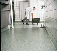 A non slippery flooring coat protects kitchen worker as he briskly moves a rolling bucket across open hallway.