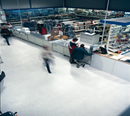 Patrons of large purchasing warehouse briskly move in seamless motion across non slip flooring.