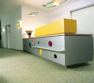 Lobby of pharmaceutical company has grey floor and yellow reception desk.