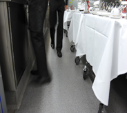 Restaurant waiters and waitresses hurriedly walk across grey colored flooring.
