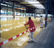 Professional floor resurfacing specialist spreads self leveling compound inside large industrial building.