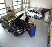 A dealership mechanic works on car atop blue floor.