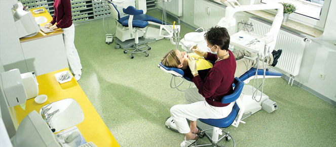 Dentist office with green flooring and a child in the dental chair having her teeth fixed.