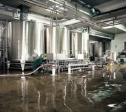 Dark earth toned concreted flooring with high glossed sealing top coat reflects lighting cast from large industrial holding tanks.