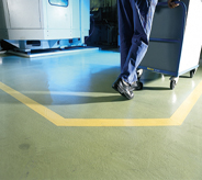 Warehouse worker pushes rolling equipment across covered concrete flooring.