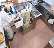 Worker cleans deli equipment on a red flake floor.