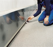 Floor installer works to complete his commercial projects by applying finishing touches to base trim.
