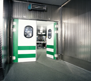 Large green and white stainless steel door reveals seamless flooring transition between interior and exterior freezer areas.