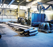 Large industrial materials rest atop chalk blue colored flooring inside a fabrication plant.