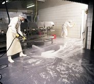 Food processing workers pressure wash interior work space protected with no slips flooring.
