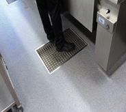 A restaurants floor grate supports standing waiter in black pants and shoes.