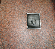 Small sized square french drain sits center of multicolored riverrocked floor.