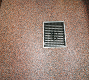 Small sized square french drain sits center of multicolored riverrocked floor.