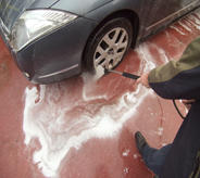 Patron of car wash pressure washes tires subsequently dowsing surrounding water proofed floor system.